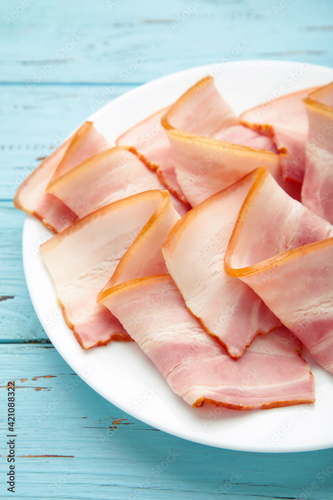 Fresh raw slices bacon on plate on blue wooden background. Fresh raw slices bacon on plate on blue wooden background.