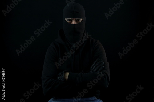 Portrait man with balaclava sitting with crossed arms looking at the camera. Crime concept