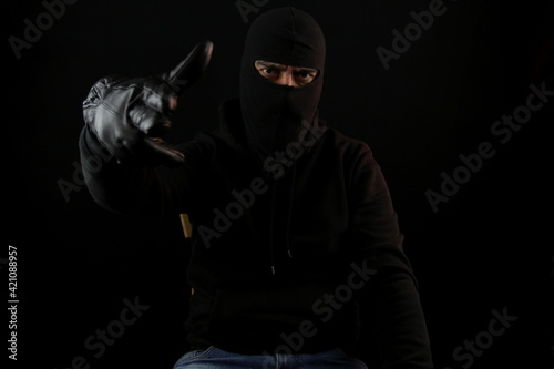 Man with balaclava sitting making the gun gesture with hand and fingers looking at the camera. Crime concept