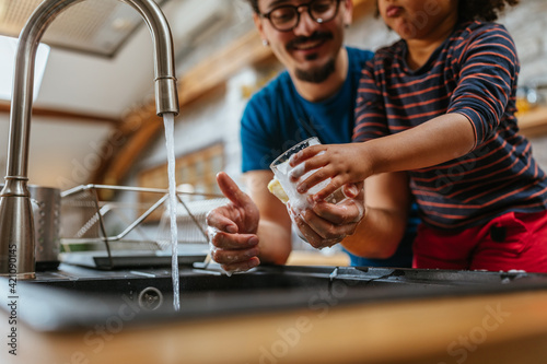 Multiracial father and daughter washing dishes together photo