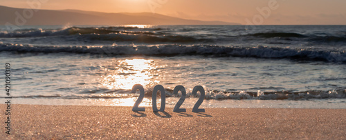 Numbers 2022 on golden sand of beach and blurry sea sunrise or sunset. New Year's vision, dreams, goals concept. New Year's Eve travel. Banner for web, selective focus, copy space
