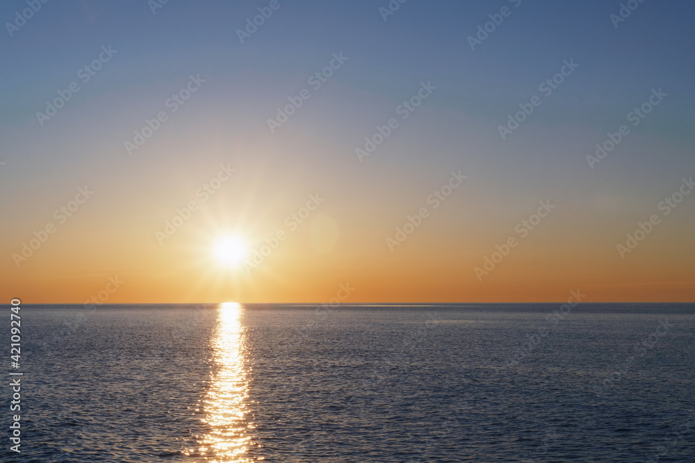 Fototapeta premium The setting sun goes into the sea on the horizon with a light track and reflections on the sea.