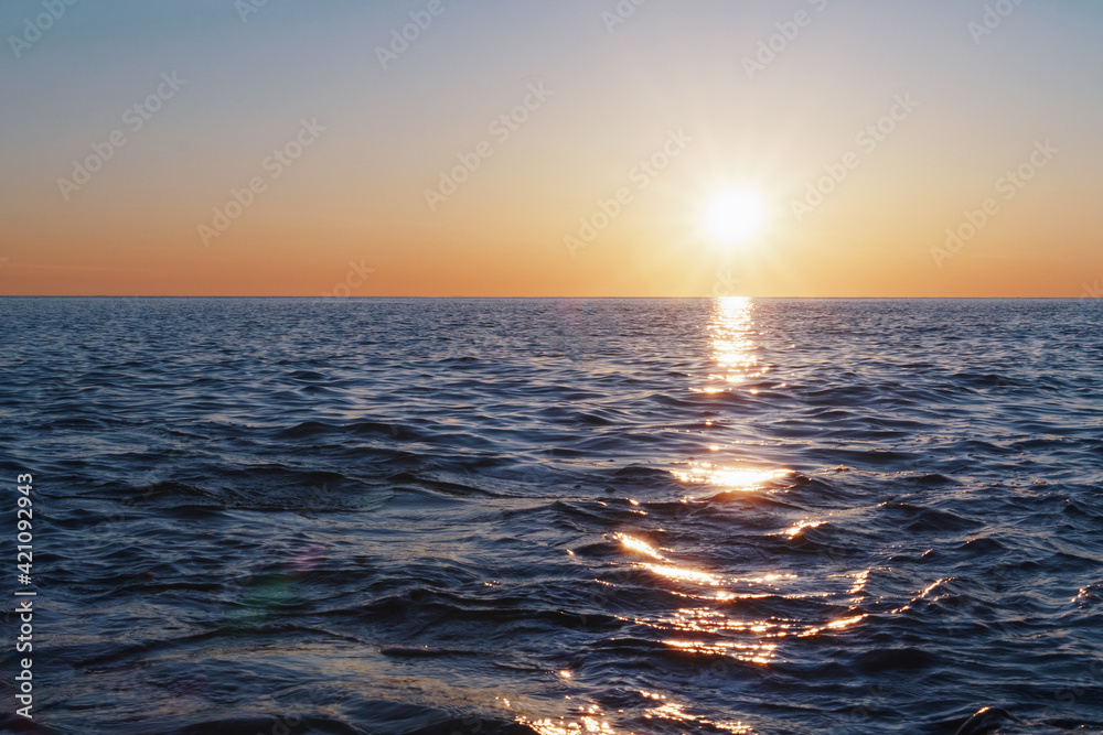 The setting sun goes into the sea on the horizon with a light track and reflections on the sea.