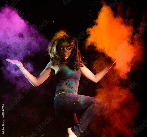 Attractive girl dances in the clouds of dry colorful holi powder on a night background. Holi festival india