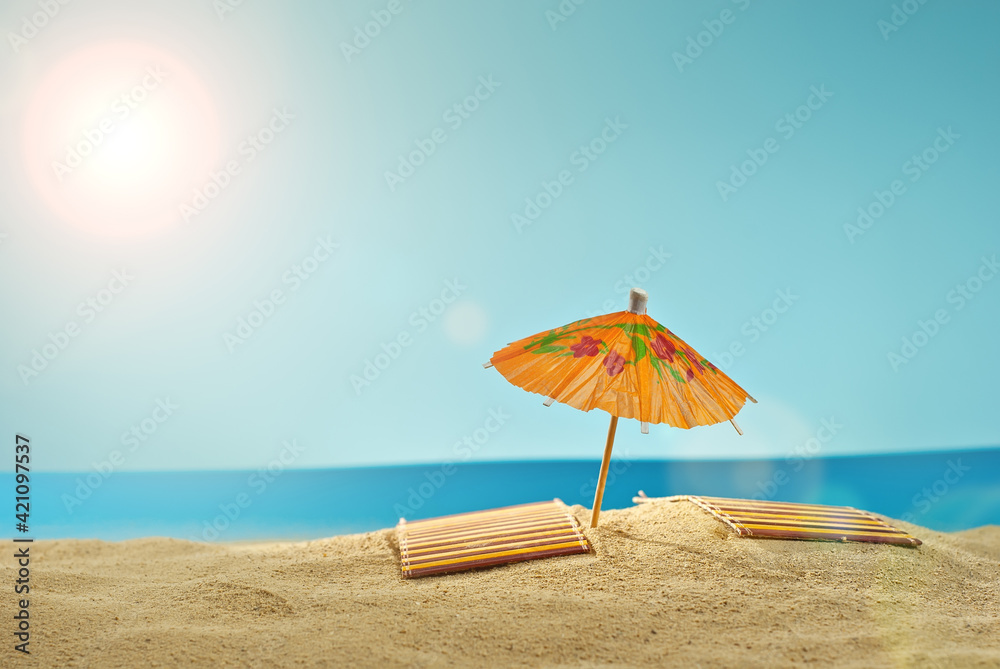 Beach umbrellas and sunbeds on the sand. Stylized cardboard beach. Paper umbrellas for cocktails in the background. The concept of rest, sea and vacation. Artificial wooden deck chairs.