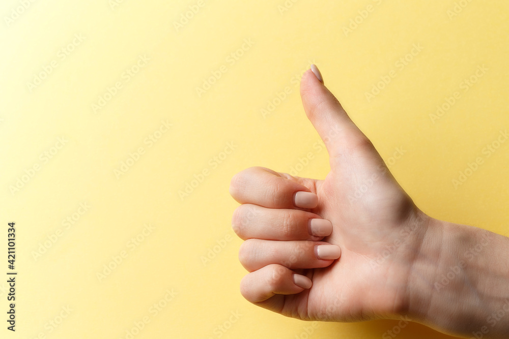 Female hand shows a like sign by holding her thumb up on bright yellow background. Girl shows like. Copy space