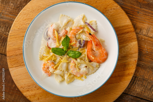 Farfalle pasta with shrimps in a creamy sauce on a gray plate on a wooden table on a round wooden stand.