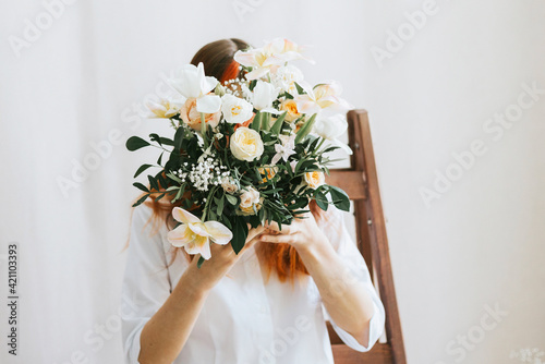 a teenage girl closed her face with a bouquet of flowers in a studio with lots of bouquets photo