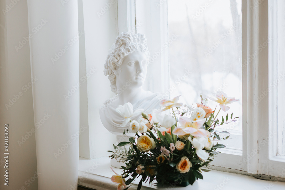 A statue of a bust of a woman stands on the window next to a bouquet of flowers, a concept of spring and International Women's Day A statue of a bust of a woman stands on the window next to a bouquet of flowers, a concept of spring and International Women's Day