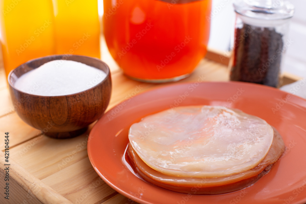Set for preparing homemade fermeted drink. Glass gar with komucha, bottle with ready beverage, black tea brew, bowl of sugar and plate with scoby. Selective focus Set for preparing homemade fermeted drink. Glass gar with komucha, bottle with ready beverage, black tea brew, bowl of sugar and plate with scoby. Selective focus
