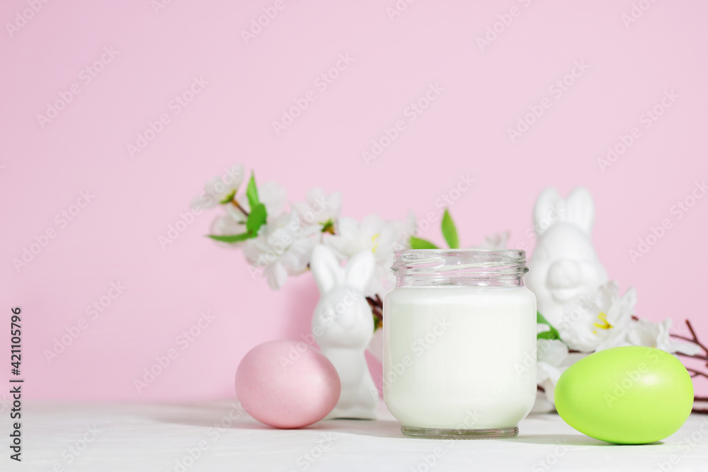 Organic probiotic milk kefir drink or yogurt in a glass container, with colored Easter eggs, on a pink background with a rabbit. Easter concept. Cold fermented milk drink with probiotics. Organic probiotic milk kefir drink or yogurt in a glass container, with colored Easter eggs, on a pink background with a rabbit. Easter concept. Cold fermented milk drink with probiotics.