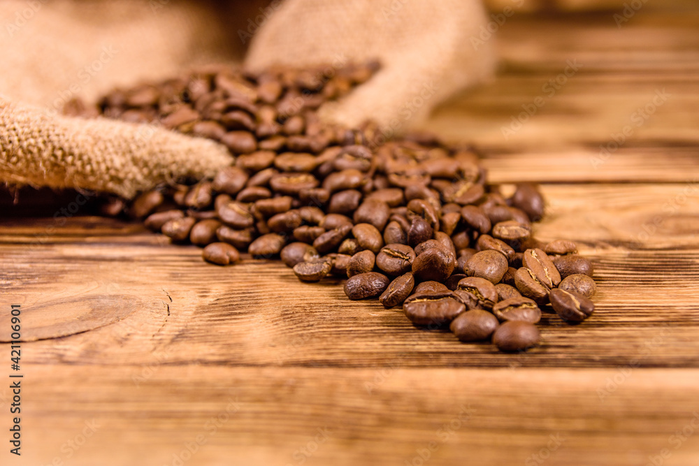 Sackcloth and scattered coffee beans on wooden table Sackcloth and scattered coffee beans on wooden table