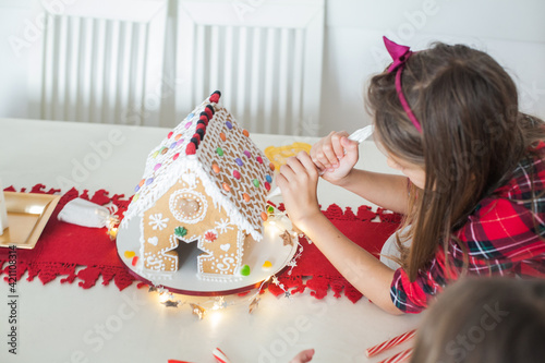 Little girl decorating Christmas gingerbread house at home