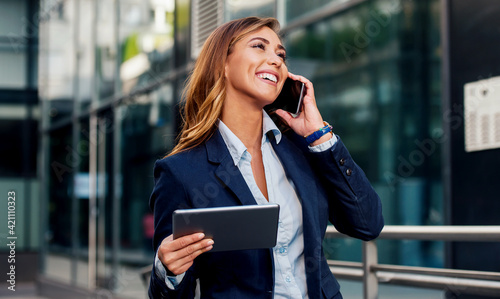 Businesswoman holding tablet and making a phone call in front of the corporation. Business, lifestyle concept photo