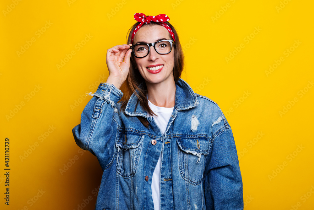 Friendly young woman in a hair band, in a denim jacket holding glasses on a yellow background. Friendly young woman in a hair band, in a denim jacket holding glasses on a yellow background.