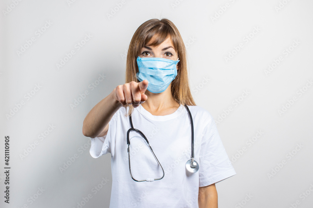 Young woman in medical mask and stethoscope pointing finger on a light background. Banner. Concept doctor, high level medical medicine, vaccination, visit to the doctor Young woman in medical mask and stethoscope pointing finger on a light background. Banner. Concept doctor, high level medical medicine, vaccination, visit to the doctor
