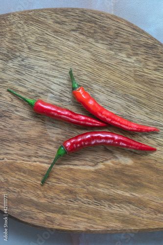 three red hot chili peppers on a wooden board. View from above