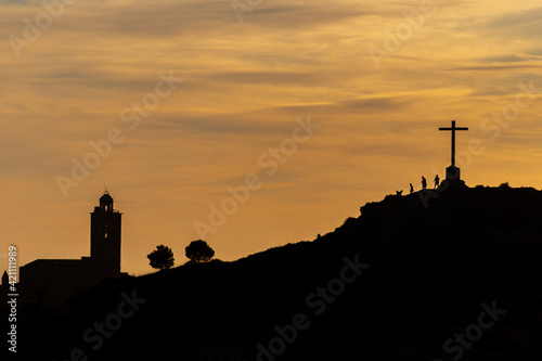 family silhouettes on the top of a hill under a large cross looking at a church