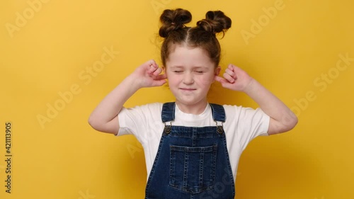 Portrait of annoyed little preschool girl close plug ears scream loudly tired by noisy sound, furious small child, avoid ignore unbearably loud noise ask quiet, isolated on yellow studio background photo