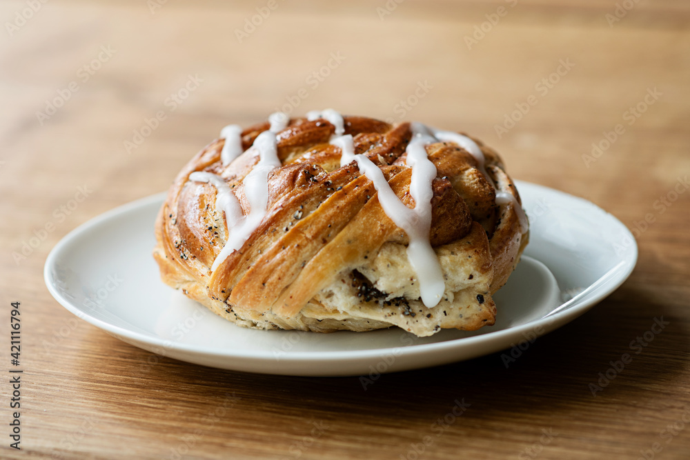 Freshly baked cinnamon roll (also cinnamon bun or cinnamon swirl) with icing on white plate on wooden table. Freshly baked cinnamon roll (also cinnamon bun or cinnamon swirl) with icing on white plate on wooden table.