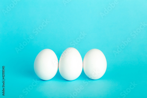  Eggs minimal concept. White funny eggs for breakfast on a colored blue background