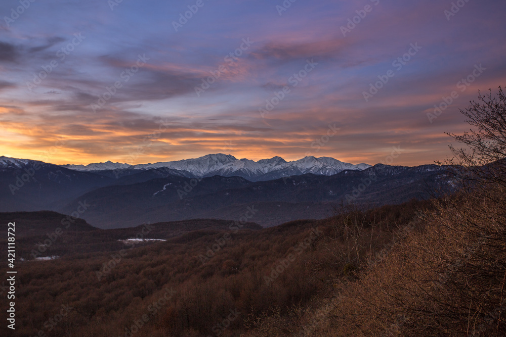 Morning landscape in the mountains of Adygea. View of the valley and snowy peaks against a background of blue sky and pink clouds. The sun rises behind the Caucasus mountains
