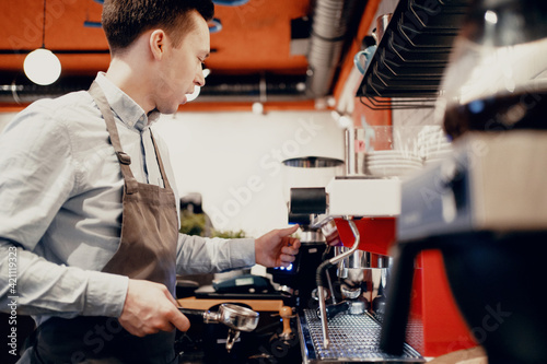 Works in his small business restaurant cafe. A male waiter makes coffee with a takeaway. Clothing apron uniform of the bar staff. Copy space. Modern interior.
