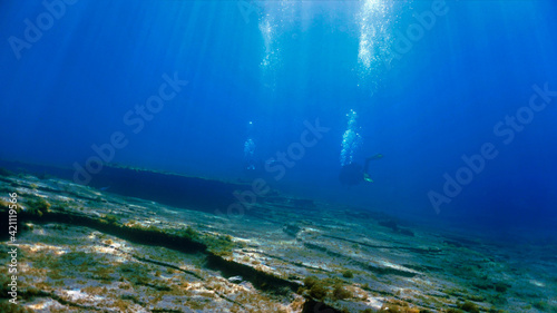Beautiful underwater landscape in sunlight with scuba divers.