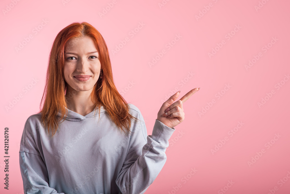 Redhead girl showing index finger to the side for copyspace in studio on pink background Redhead girl showing index finger to the side for copyspace in studio on pink background
