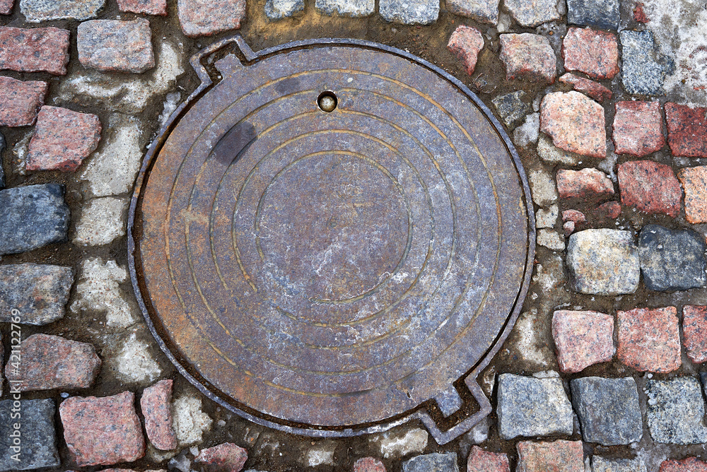 Detail of granite street paving stones in blue and brown colors. Old manhole cover.