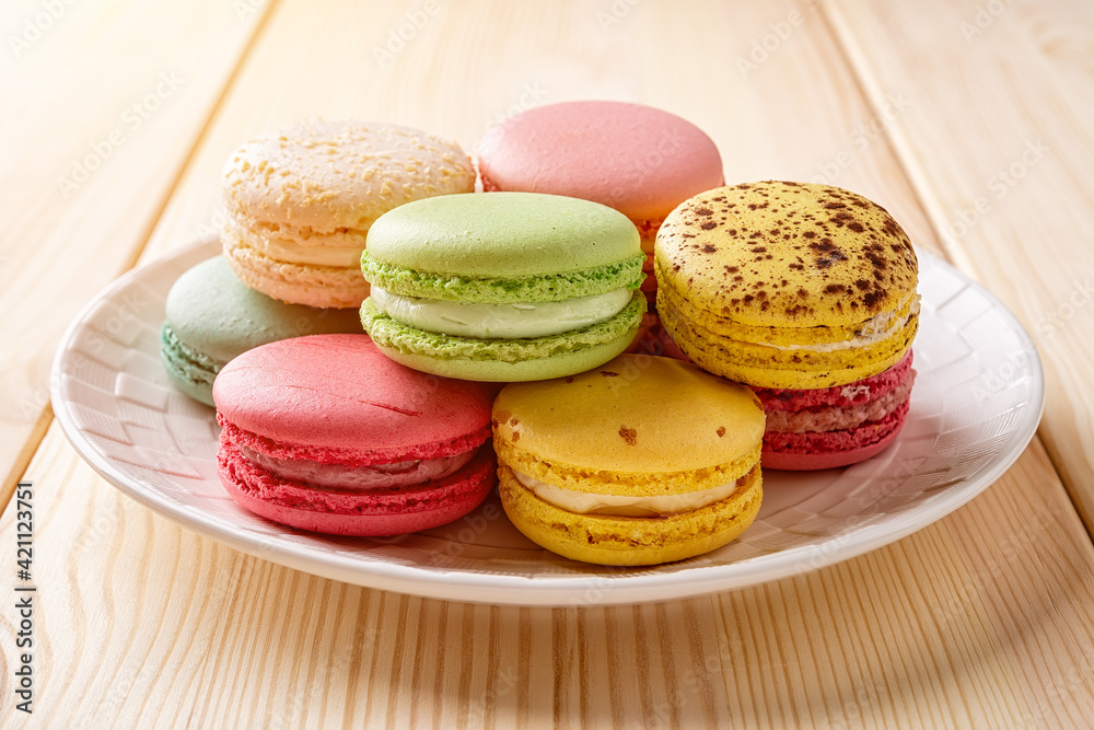 Set of multicolored macaroons on a white plate over wooden table. Colorful macaron cakes variety. Delicious french dessert. Sweets of almond flour with a delicate cream.