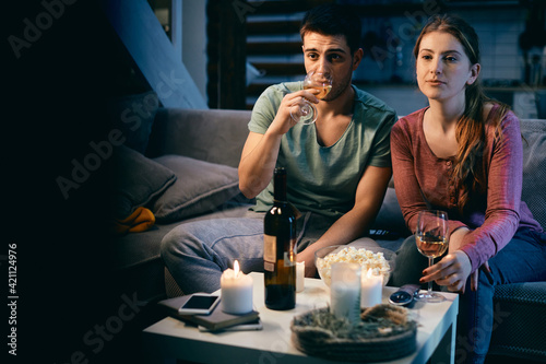 Young couple drinking wine while watching TV at night at home.