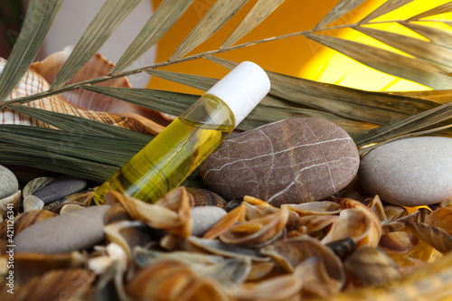 A bottle of aromatic oil lies among shells, stones and dried plants on a yellow background, close-up