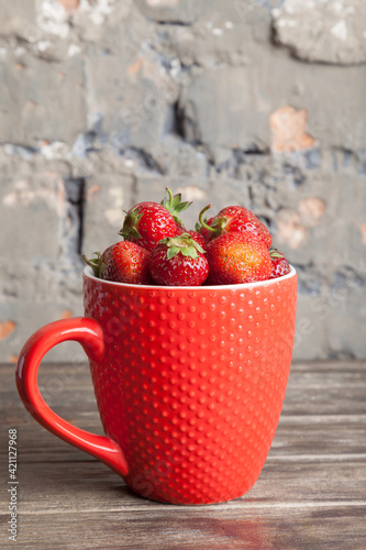 Fresh organic strawberry in red cup on wooden background. Healthy breakfast. Natural farming. Growing fruit. 