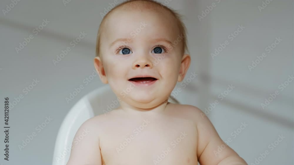 Stock Little naked baby boy smiling. Portrait of happy caucasian toddler sitting against grey wall with shadow play. | Adobe Stock