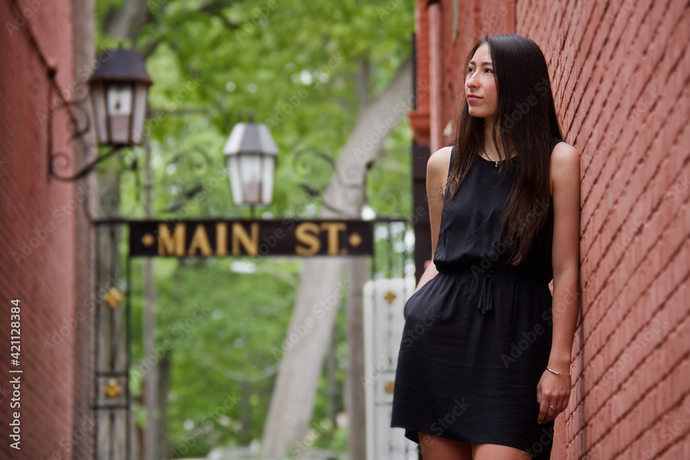 Outdoor portrait of beautiful young woman in sleeveless black dress in main street urban setting