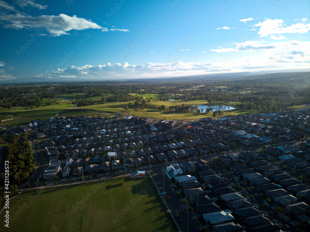 Fototapeta premium Aerial photograph of suburban sporting field and housing estate at sunset, with blue sky and white clouds.