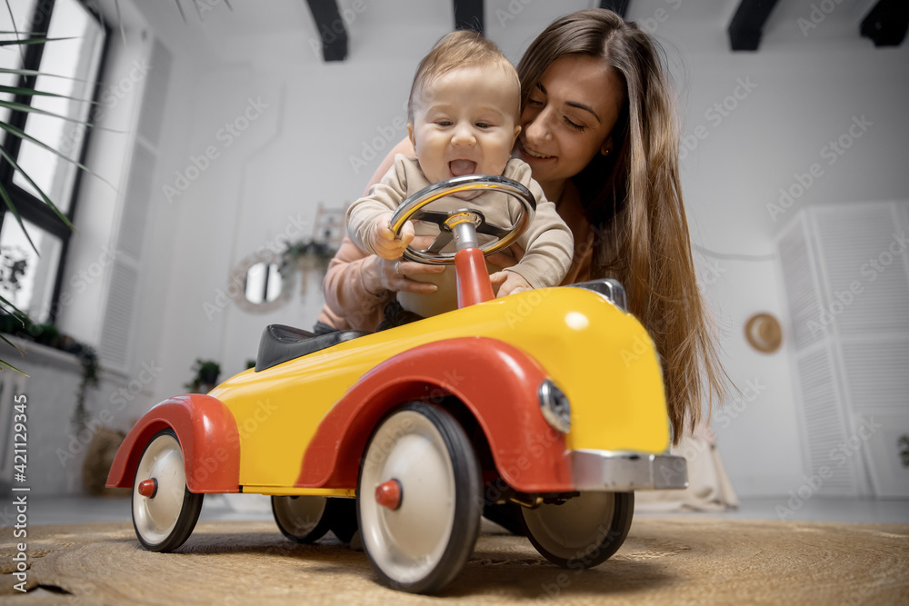Concept Young baby driver. Mother plays with her little son and big toy car, boy holds steering wheel and laughs Concept Young baby driver. Mother plays with her little son and big toy car, boy holds steering wheel and laughs