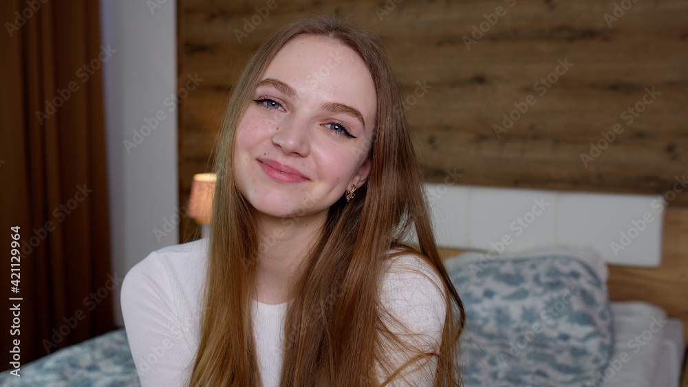 Smiling pretty young woman in good mood looking at camera, smiles gently on bedroom background Smiling pretty young woman in good mood looking at camera, smiles gently on bedroom background