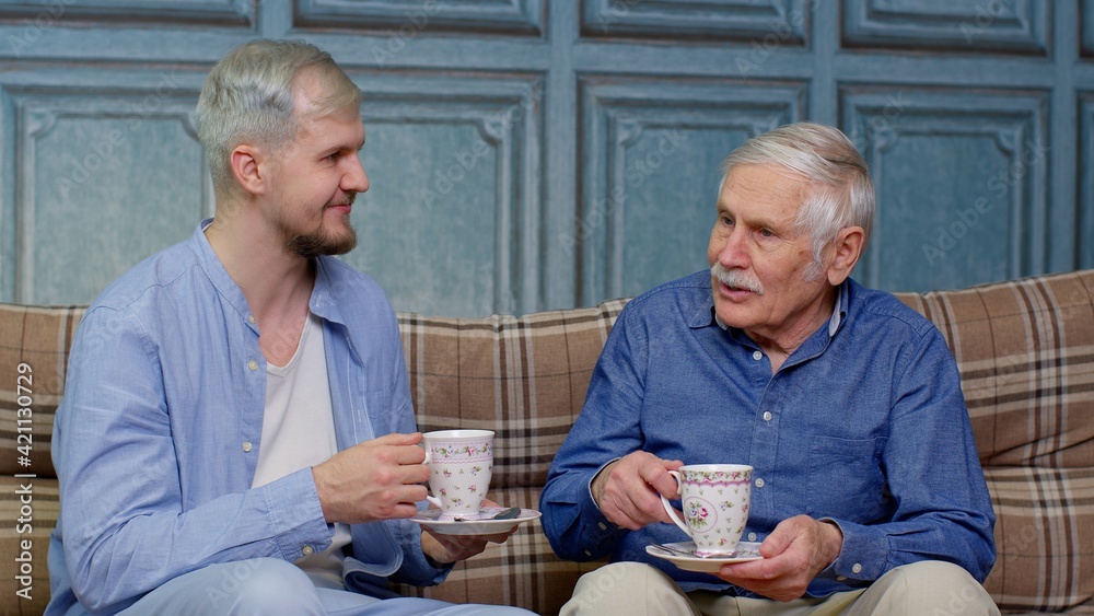 Different male generations family of senior father and adult son or grandson relaxing, drinking tea
