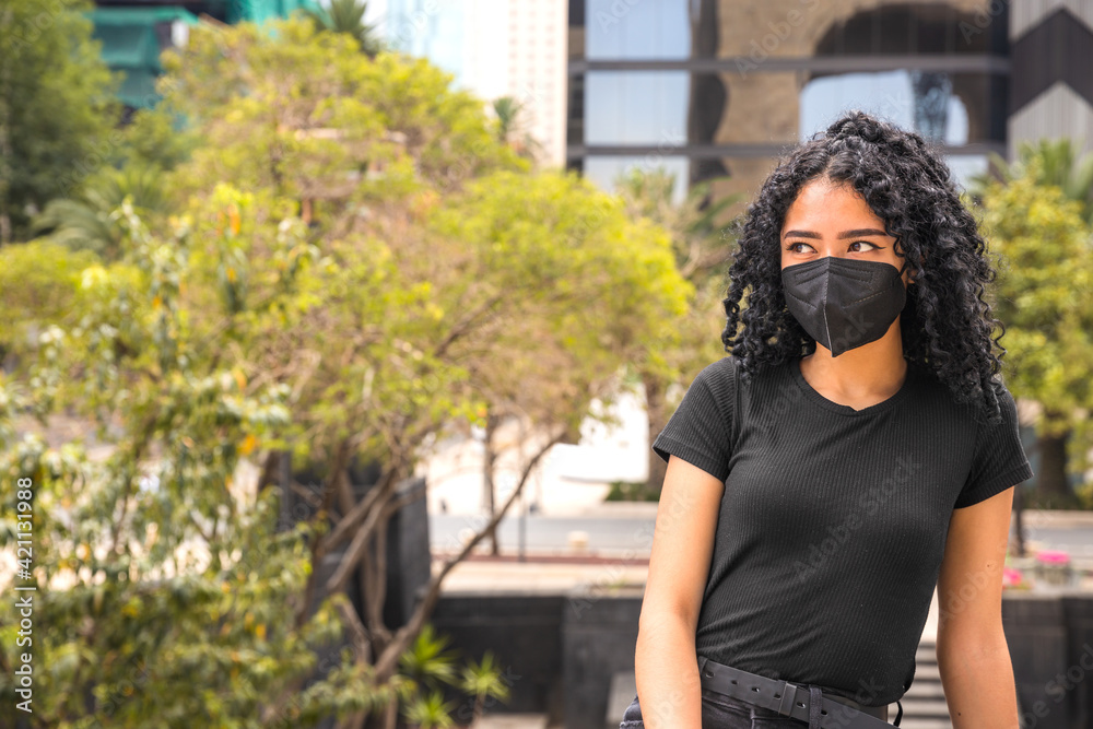 Young woman with curly hair is sitting. He is wearing a black mask Young woman with curly hair is sitting. He is wearing a black mask