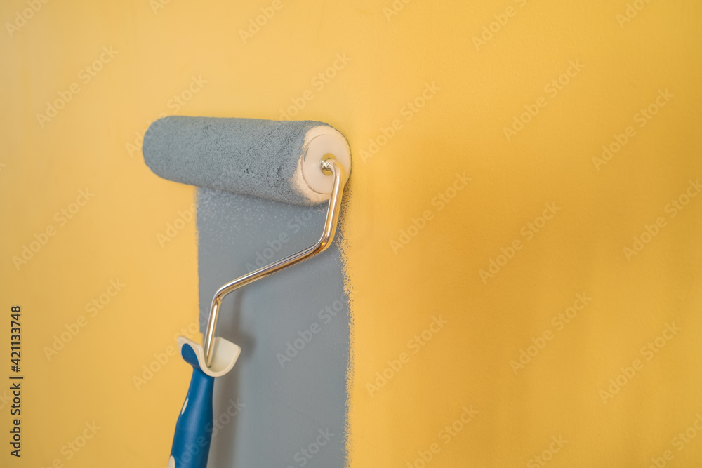 Obraz premium Paint Roller with Blue Paint on a Yellow Wall