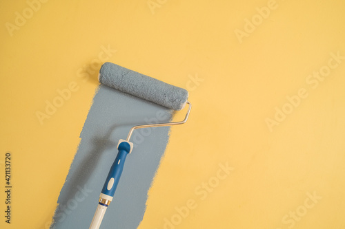 Paint Roller with Blue Paint on a Yellow Wall