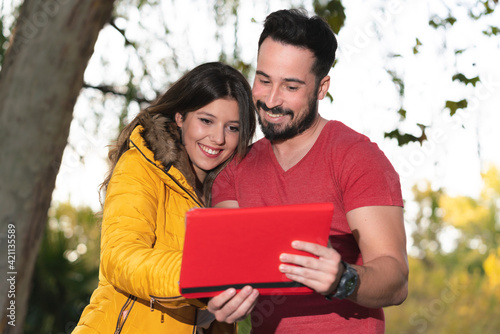 Cute couple watching a movie smiling on a tablet in a park