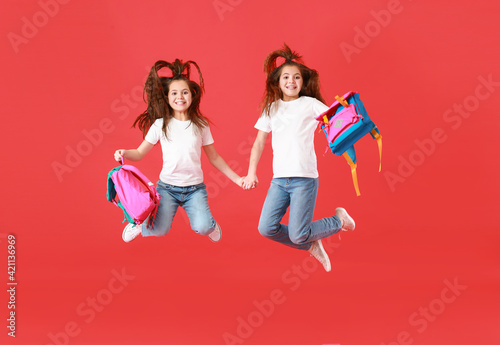 Jumping twin school girls on color background