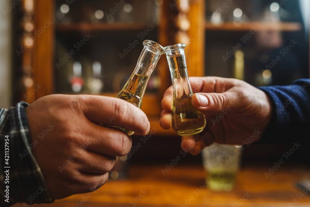 Close up on hands of two unknown men toasting with traditional serbian drink plum brandy rakija slivovitza holding glass called cokance at home