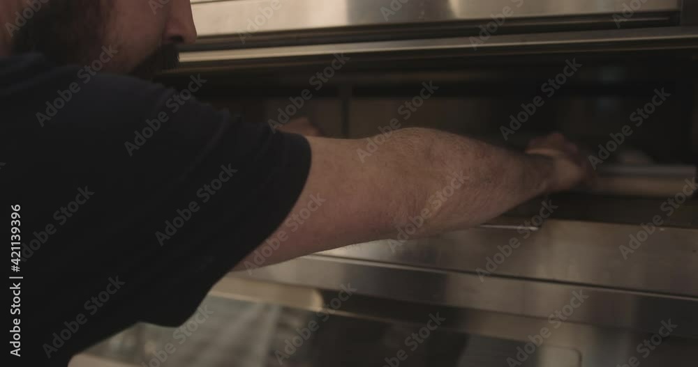 Bearded male baker putting artisan baguettes in oven working in industrial bakery Bearded male baker putting artisan baguettes in oven working in industrial bakery