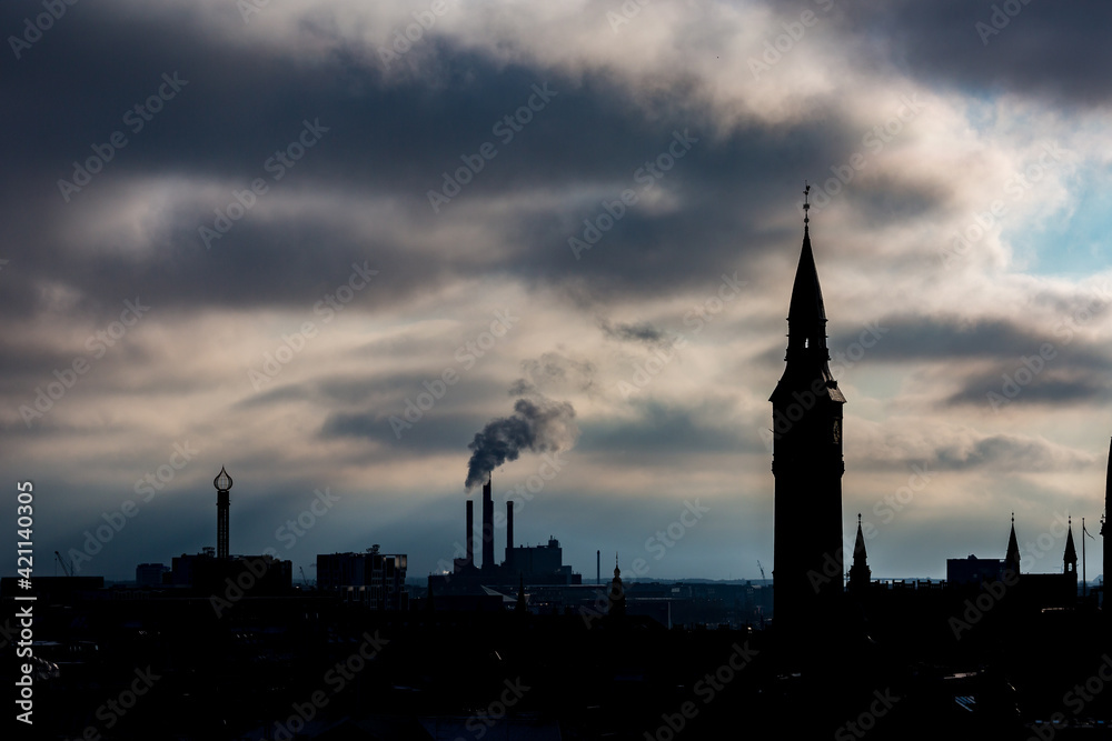 Cityscape, amazing silhouettes view over the city of Copenhagen, Denmark. Winter cloudy dark moody picturesque scene. Picture taken from Round Tower. Church tower and smoking chimneys