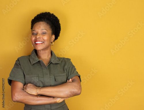 black woman smiling in a green outfit and arms crossed on a yellow background