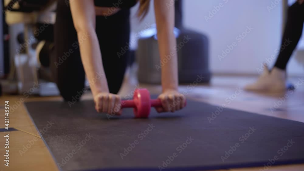 Confident slender fit woman using rolling dumbbell in gym working out. Portrait of concentrated Caucasian slim sportswoman training exercising indoors. Beauty and sportive lifestyle. Confident slender fit woman using rolling dumbbell in gym working out. Portrait of concentrated Caucasian slim sportswoman training exercising indoors. Beauty and sportive lifestyle.